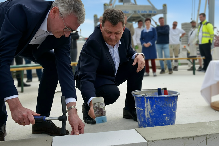 Carsten Reeck (links) und Christoph Domke (rechts) setzen gemeinsam den Grundstein für den Bau des neuen Bürogebäudes.